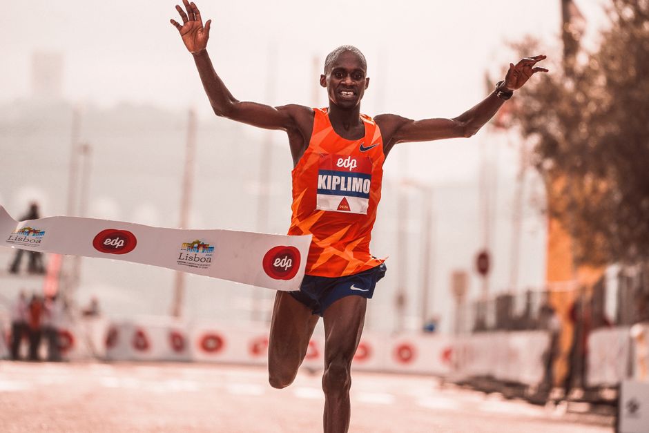 Marathon runner finishes race with arms raised in Lisbon, captured mid-stride at the finish line.